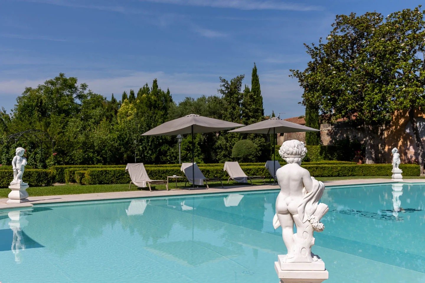 Sun loungers and parasols beside the pool, cypresses beyond