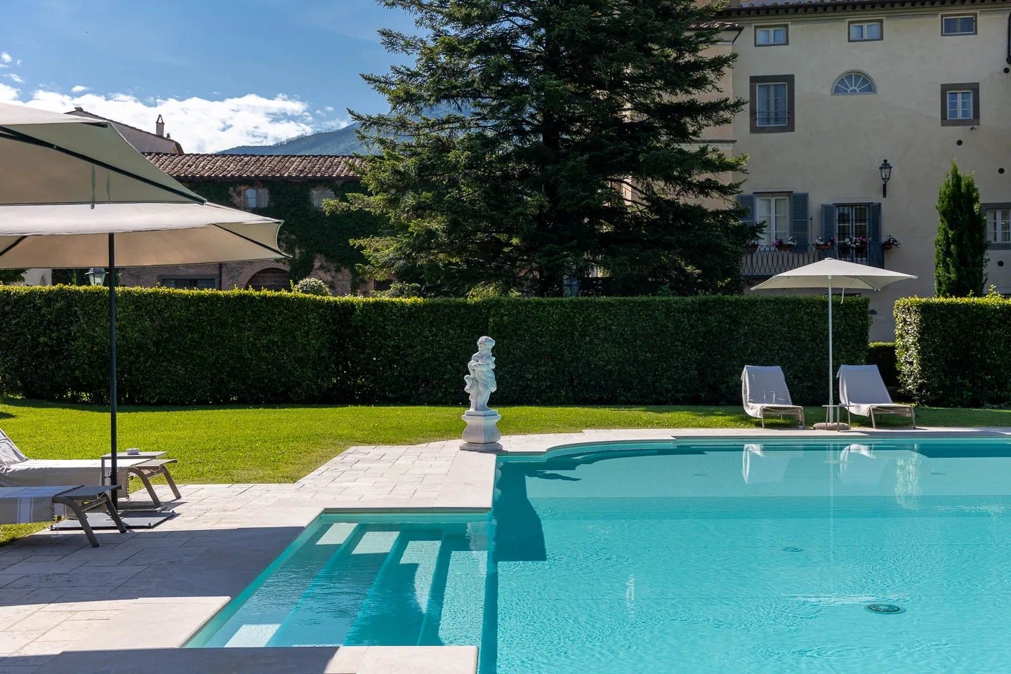 The pool on the lawn, a statue at one corner and the villa behind