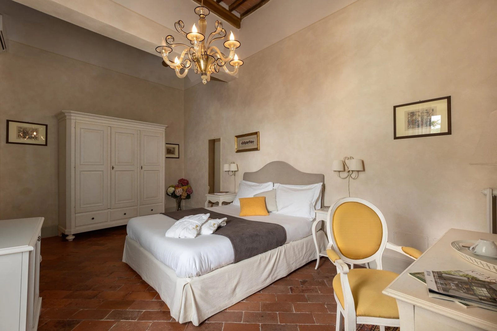 A bedroom in the main house — chandelier, terracotta floor, tall shuttered windows