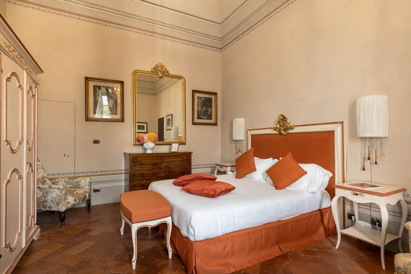 A bedroom with a terracotta bedspread, a gilt mirror and an antique chest of drawers