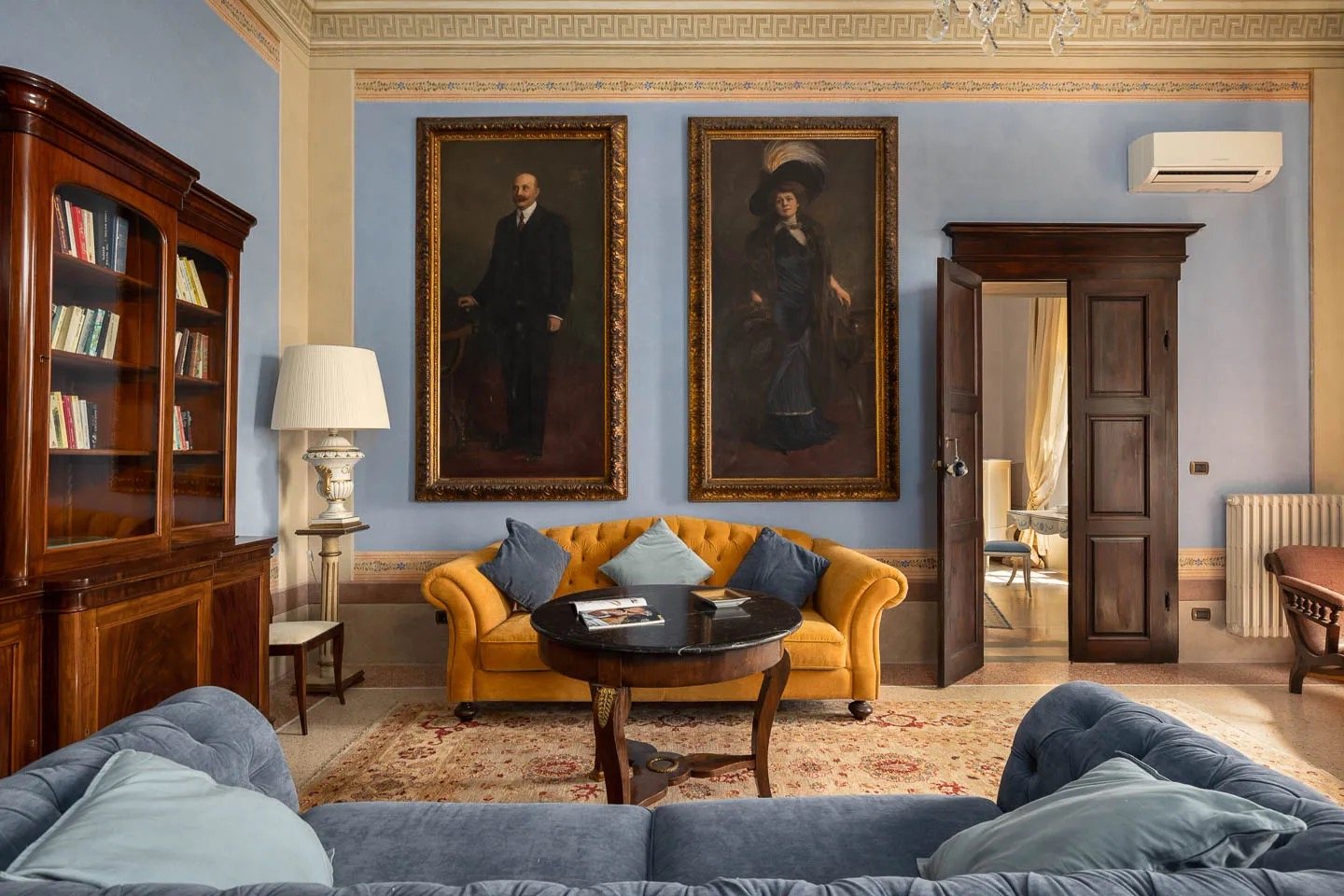 The salon: two large family portraits above a velvet sofa, rugs over a tiled floor
